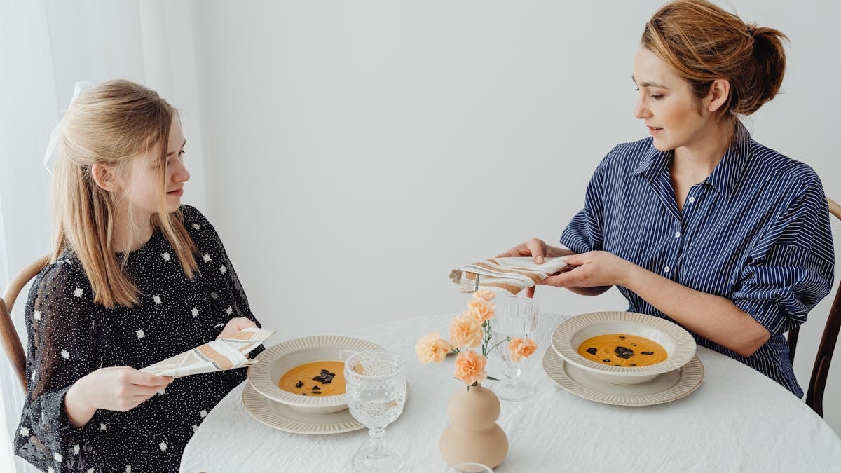 Two women dining with soup at an elegantly set table.